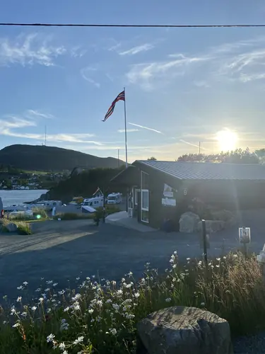 Kveldssol over resepsjonsbygget og flaggstanga, med villblomster i forgrunnen