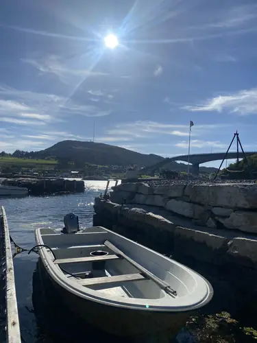 En utleiebåt ved brygga med sola høyt over Boknasundet
