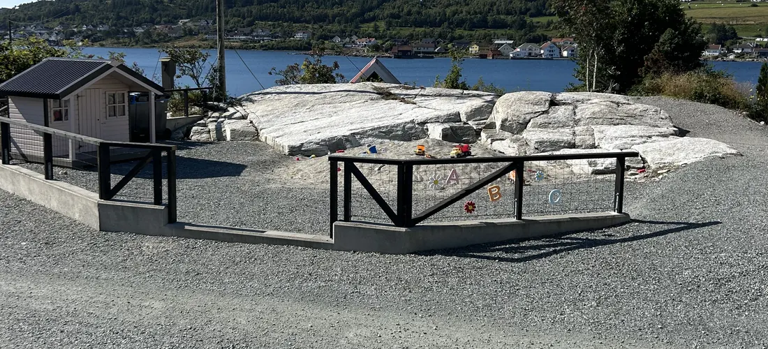 Lekeplassen på campingplassen, med inngjerdet sandkasse på svaberget, lekehus og sundet bak